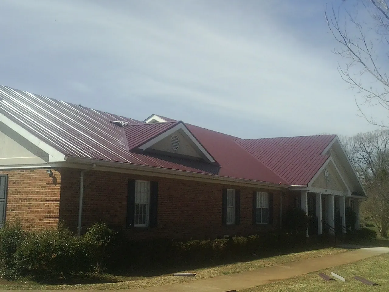 Red metal roof with gabled entries on a long brick building, from a Hail Damage Roof Repair job in Millmont
