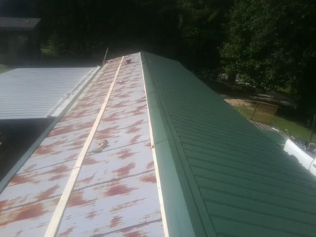 Old rusted panels beside newly installed green metal roofing — Wind Damage Roof Repair by Roofing Brothers in Millmont
