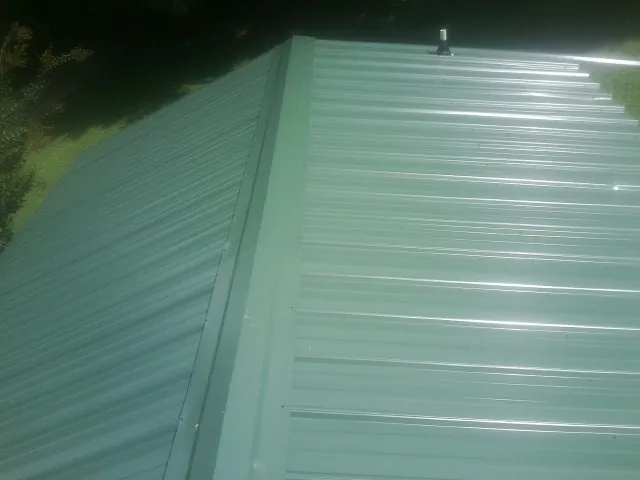 New green metal panels meeting at the ridge of a roof — Flat Roof Repair work by our crew in Millmont