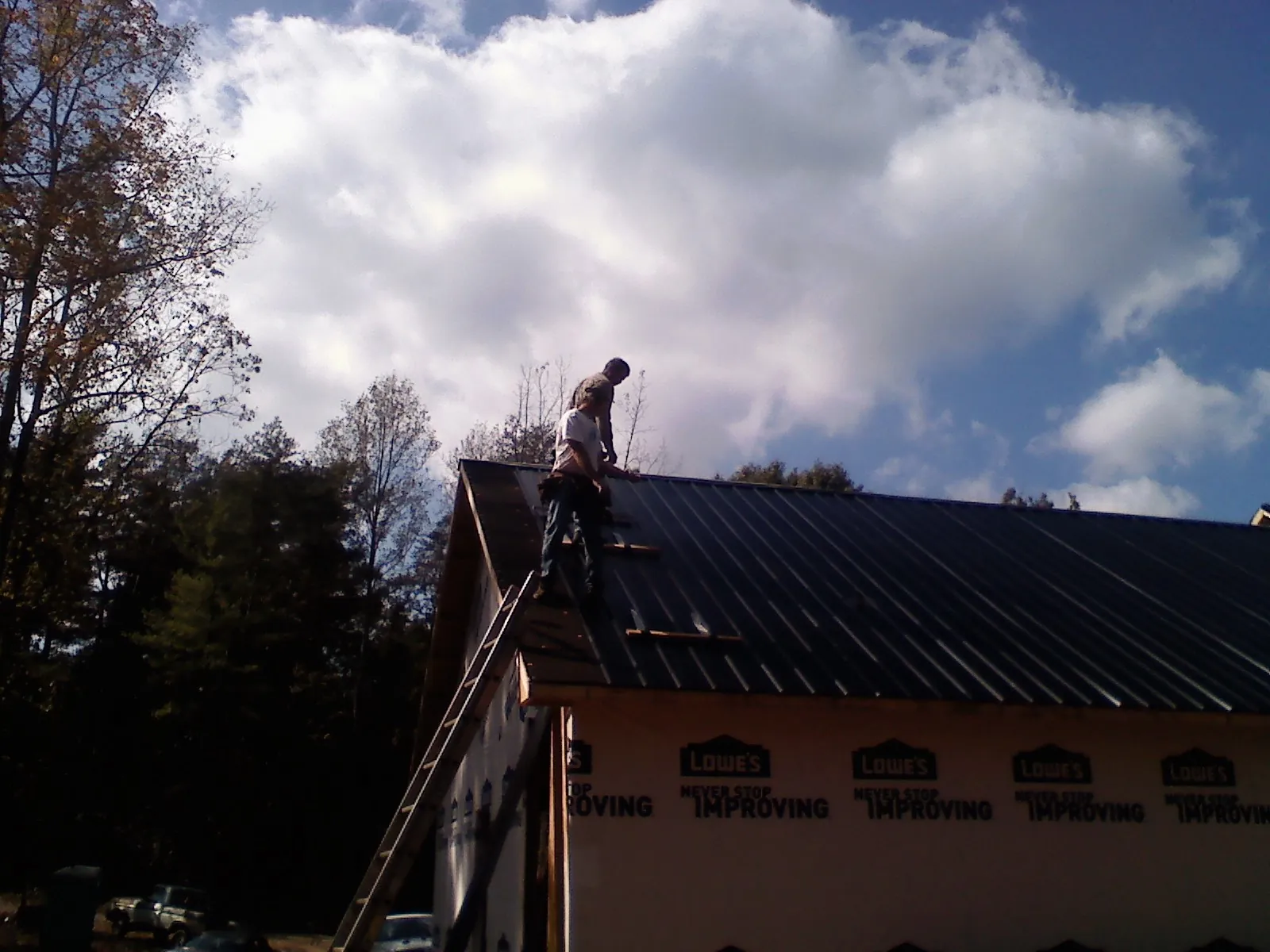 Roofer fastening dark metal panels high against a cloudy sky, from a Roof Inspection job in Millmont