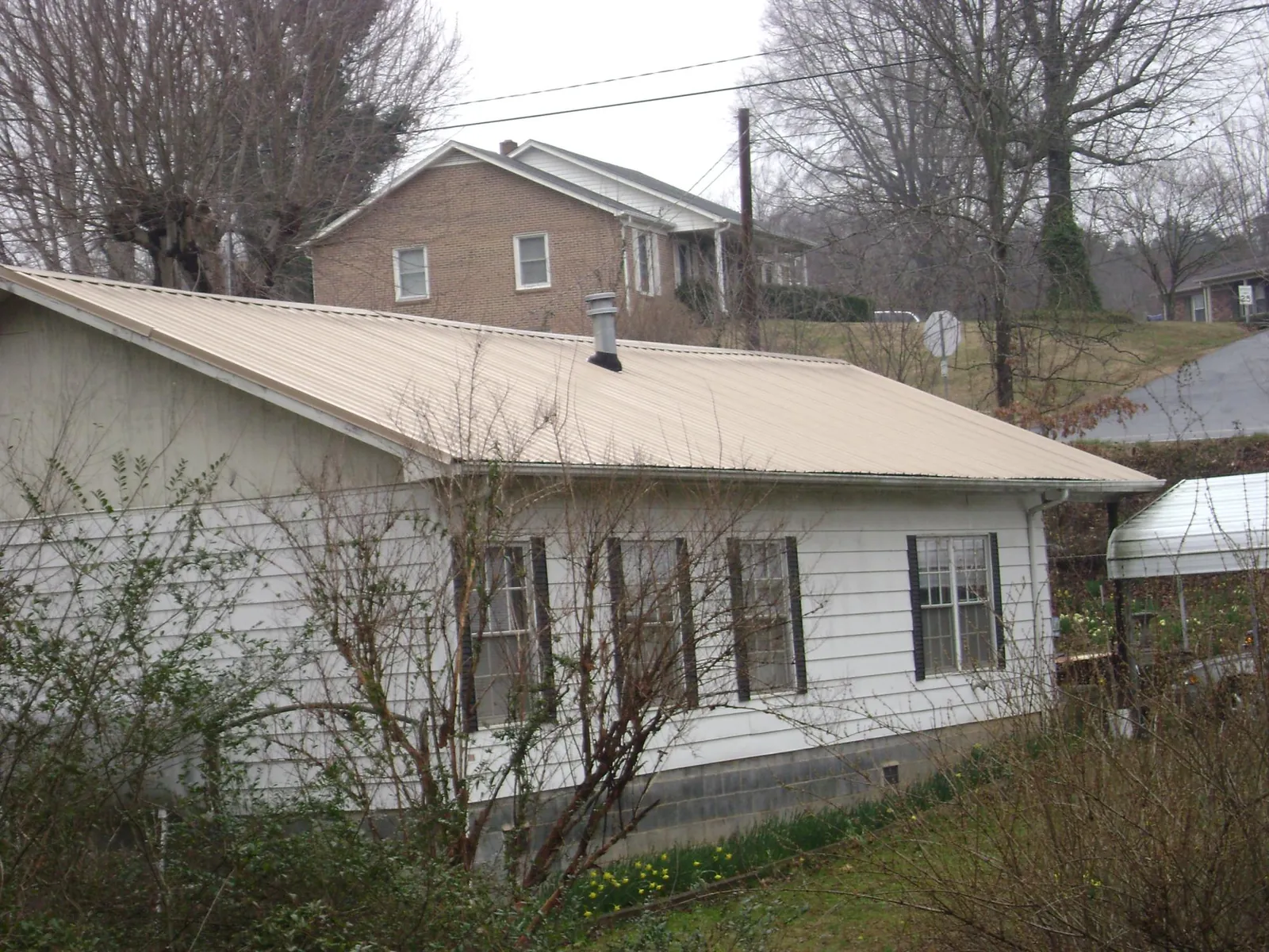 Tan metal roof on a white sided house set into a hillside — Commercial Roofing by Roofing Brothers in Millmont